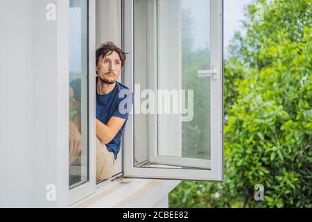 Extrem müde junger Mann, der aus dem Fenster schaut, allein zu Hause. Selbstisolation zu Hause, Quarantäne wegen Pandemie COVID 19. Psychische Probleme in Stockfoto