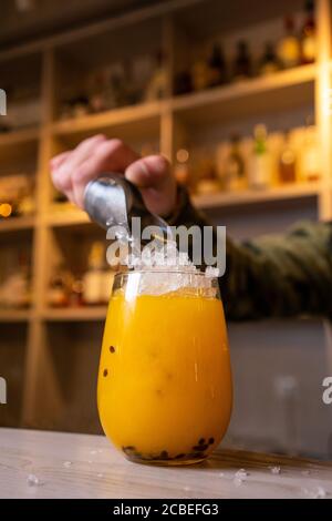Alkoholgetränke, Menschen und Luxuskonzept - Barkeeper mit Glas und Zitronenschale, der Cocktail an der Bar zubereitet Stockfoto
