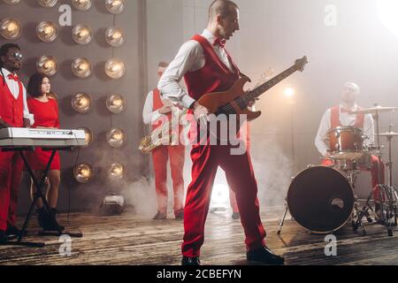 Hübscher Mann mit Gitarre, während er auf der Bühne tssanding.Probe vor dem Festival. Foto in voller Länge Stockfoto