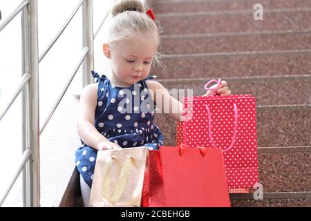 Kleines Mädchen sitzt mit farbigen Taschen auf den Stufen in der Mall. Stockfoto