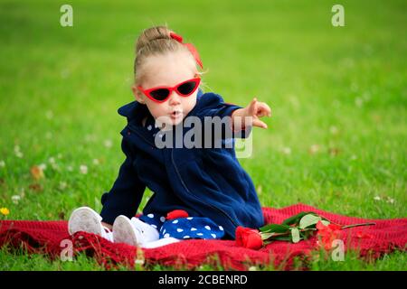 Kleines Mädchen sitzt auf dem Gras im Park tragen Sonnenbrille Stockfoto