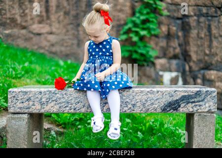 Junge blonde Mädchen auf einer Bank mit einer Rose sitzen Stockfoto