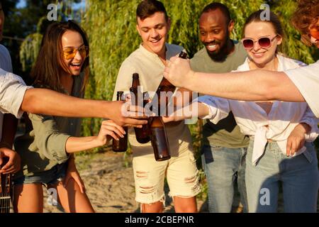 Vibes. Eine Gruppe von Freunden klirren Biergläser während Picknick am Strand in der Sonne. Lifestyle, Freundschaft, Spaß haben, Wochenende und Ruhe Konzept. Sieht fröhlich, glücklich, feiern, festlich. Stockfoto