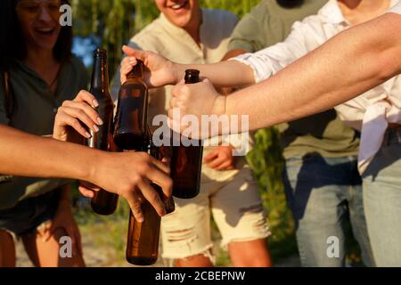 Vibes. Eine Gruppe von Freunden klirren Biergläser während Picknick am Strand in der Sonne. Lifestyle, Freundschaft, Spaß haben, Wochenende und Ruhe Konzept. Sieht fröhlich, glücklich, feiern, festlich. Stockfoto