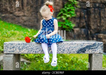 Ein junges Mädchen in einem blauen Kleid mit einer Rose In ihren Händen sitzt auf einer Bank im Park Stockfoto