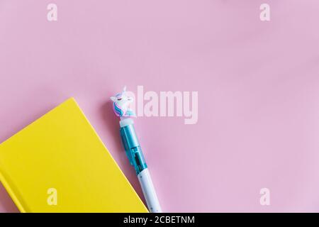 Gelbes Notizbuch für Notizen, lustiger Einhorn-Stift auf rosa pastellfarbenem Hintergrund. Flach liegend. Draufsicht. Speicherplatz kopieren Stockfoto