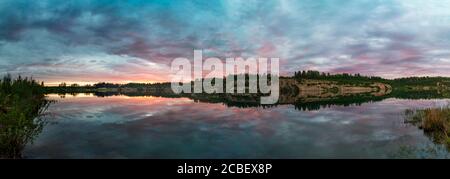 Wolken sind bei Sonnenuntergang über dem See in verschiedenen Schattierungen gefärbt. Stockfoto