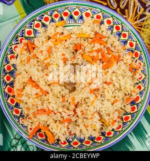 Orientalische Küche. Usbekischer Pilaf oder Plov von Reis und Fleisch in einem Teller mit einem ethnischen Muster. Blick von oben. Stockfoto