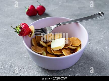 Trendiges Essen - Pfannkuchen Müsli. Haufen Mini-Cerealien-Pfannkuchen mit Erdbeeren und Butter in rosa Boul. Stockfoto