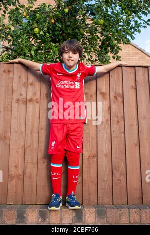 Der neunjährige kaukasische Junge steht an einer Außenwand und trägt das von Nike entworfene 2020/21 Home Liverpool Football Club Trikot. Lancashire UK Stockfoto