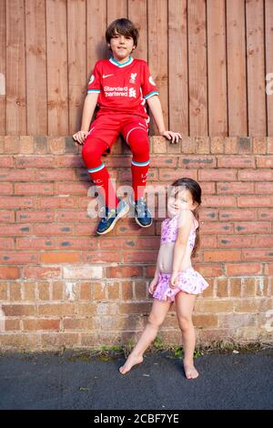 Der 9-jährige kaukasische Junge und die jüngere Schwester sitzen im Sommer 2020 auf einer Ziegelwand. Lancashire, Großbritannien Stockfoto