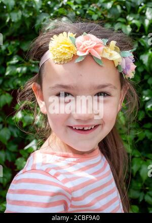 Kopf- und Schulterportrait eines 4-jährigen weißen Mädchens, lächelnd, mit künstlichen Blumen im Haar. Lancashire, England, Großbritannien Stockfoto