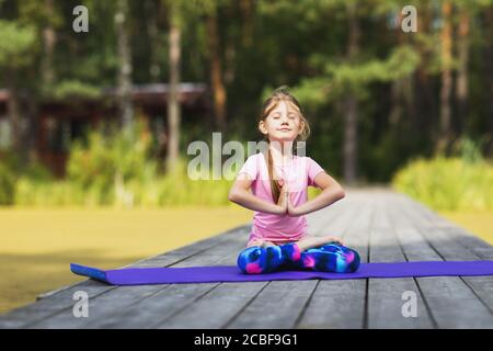 Das kleine Mädchen meditiert im Park und sitzt in der Lotusposition auf einer Holzbrücke. Konzept zum Thema Yoga für Kinder Stockfoto