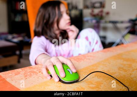 Das Mädchen steuert die Computermaus. Das Kind sitzt zu Hause auf einem Stuhl. Zu Hause studieren. Stockfoto