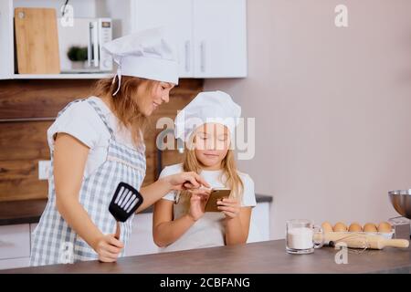 Porträt von Frau und Kind auf Smartphone vor dem Backen, Suche Rezept für Backen Stockfoto