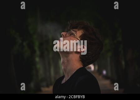 Nahaufnahme eines jungen Mannes mit Brillen und Rauch in die Luft mit verschwommenem Hintergrund Stockfoto