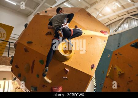 Volle Rückenansicht des unerkennbaren männlichen Boulderers, der an einer komplizierten und gefährlichen Felswand hochklettert, voller Motivation, bleibt positiv und Opti Stockfoto