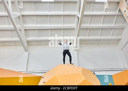 Low-Angle-Ansicht von körperlich behinderten jungen Boulderer, die an der Spitze der künstlichen Kletterwand stehen, extrem glücklich und stolz auf sich selbst, gut eq Stockfoto