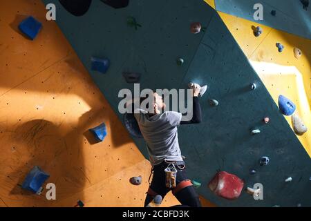 Seltene Ansicht des männlichen Boulderer mit körperlicher Behinderung nach Aufwärmübungen, Training an der bunten Kletterwand im Boulderzentrum, gesund und Stockfoto