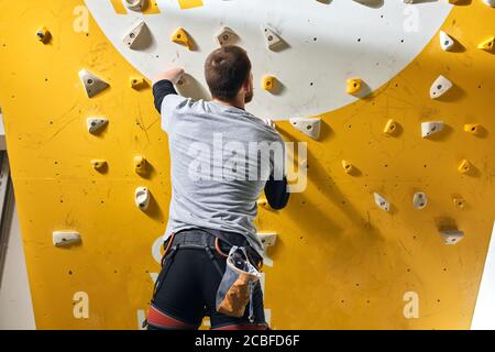 Professionelle junge männliche Kletterer mit körperlicher Behinderung Inspektion Kletterwand, Überprüfung der Fixierung von künstlichen Felsen und hält vor dem Training Stockfoto