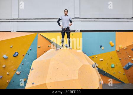 Körperlich beeinträchtigt gut aussehende männliche Modell posiert an der Spitze der Kletterwand bei Werbefotoshooting für neue moderne bunte Bouldern Sportzentrale Stockfoto