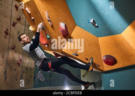 Ganzkörperaufnahme eines körperlich behinderten Bergsteigers, der in bequemen Sportkleidung Klettern im Boulderbereich praktiziert, Stockfoto