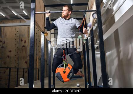 Vorderansicht des starken muskelbemuskelten Sportlers mit körperlicher Behinderung durchführen Pull-ups mit Last an seinen Beinen auf spezielle Ausrüstung Im Klettersport cente Stockfoto