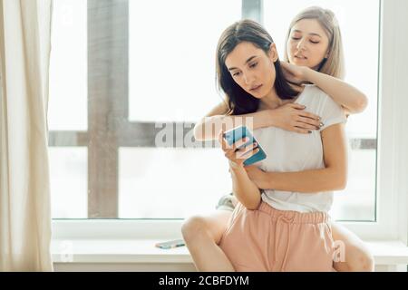 Attraktive dunkelhaarige Frau surft im Netz, während ihre kleine Schwester hinter ihr steht und streichelt ihren Kopf. Nahaufnahme Foto. Copy space, instagra Stockfoto