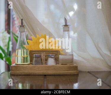 Gewürze wie Salz, Pflanzenöl, schwarzer Pfeffer, Essig und gelbe Papierservietten stehen auf einem Holzgestell auf dem Tisch vor dem Hintergrund eines Whi Stockfoto