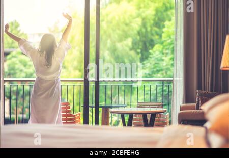 Glückliche Frau streckt und öffnet die Vorhänge am Fenster am Morgen. Süße Träume, neuer Tag, Wochenende, Urlaub Konzept Stockfoto