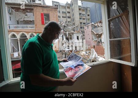 Beirut, Libanon. August 2020. Ein Mann sieht sich Fotos in seinem beschädigten Haus in Beirut, Libanon, an, 13. August 2020. Am 4. August erschütterte zwei riesige Explosionen den Hafen von Beirut, erschütterte Gebäude in der Hauptstadt des Libanon, tötete 171 Menschen und verletzte mindestens 6,000. Quelle: Bilal Jawich/Xinhua/Alamy Live News Stockfoto