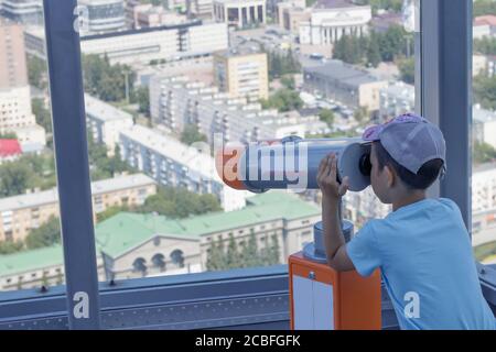 Der Junge blickt aus einem Panoramafenster eines Hochhauses auf der Stadt Jekaterinburg, Russland, in ein Teleskop Stockfoto