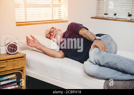 Der alte Mann lag allein zu Hause im Bett, mit der Hand, die Schmerzen in den Beinen hielt. Stockfoto