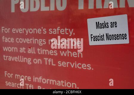 London, Großbritannien. August 2020. Ein Hinweisschild an einer Bushaltestelle, vom Bürgermeister von London und dem TfL, ist mit einem Aufkleber mit der Aufschrift "Masken sind faschistischer Unsinn", der von einem Anti-Masker aufgesetzt wurde, verunreinigt. Die Zahl der Fahrgäste im öffentlichen Nahverkehr ist weiter zurückgegangen. Diejenigen, die Reisen meist tragen Masken, nachdem sie obligatorisch auf öffentlichen Verkehrsmitteln. Die „Sperre“ für den Coronavirus (Covid 19) Ausbruch in London geht weiter. Kredit: Guy Bell/Alamy Live Nachrichten Stockfoto