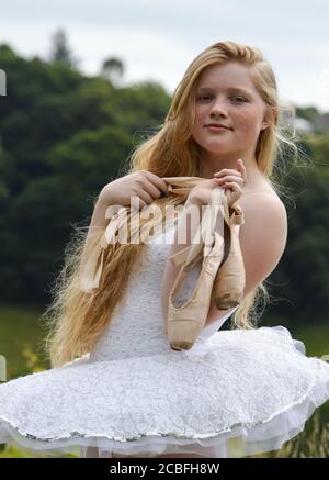 Eine Ballerina mit langen blonden Haaren und Sommersprossen starrt in die Kamera und hält ihre spitzenschuhe. Sie trägt ein weißes Tutu. Stockfoto