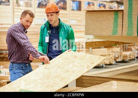 Schöner Mann Kunde Überprüfung Holzbrett auf dem Markt, er wird es für den Bau eines neuen Hauses kaufen, Lagerarbeiter helfen ihm Stockfoto