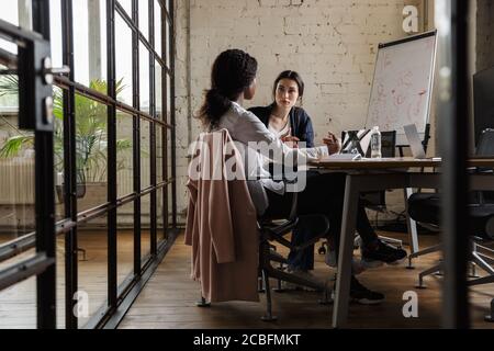Zwei attraktive, intelligente, multiethnische Unternehmerinnen, die in einem modernen Büro an einem Schreibtisch arbeiten Stockfoto