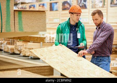 Der gutaussehende Mann konsultiert mit dem Lagerarbeiter in Uniform, deren Größe des Holzbretts geeignet sein wird Stockfoto