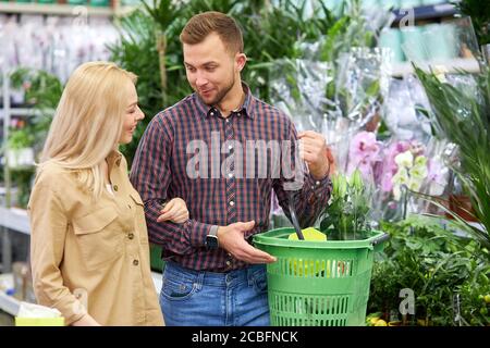 Frau shopaholic kam, um Kauf mit Ehemann zu machen, Paar kaufen Pflanzen in Töpfen, genießen Sie den Einkauf. Grüne Pflanzen und Blumen für ihre neue Wohnung Stockfoto