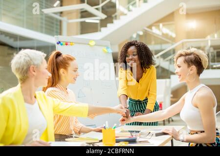 Positives Team mit eigenen Traditionen. Junge lustige Frauen in stilvoller Casual-Kleidung mit Fäusten übereinander als Symbol für ihre Partnerschaft, große t Stockfoto