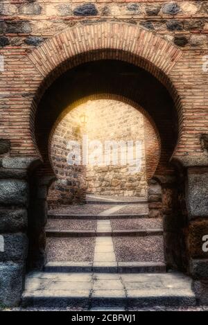 Antiker maurischer Steinbogen, der zu einer schmalen Gasse führt, die von einer alten Laterne beleuchtet wird. Architektur in Toledo, Spanien. Stockfoto