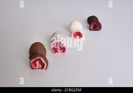 Himbeeren getaucht oder in Form Schokolade in zwei Hälften geschnitten bedeckt. Verschiedene Geschmacksrichtungen: Weiße Schokolade, Milchschokolade, dunkle Schokolade und Kekse Stockfoto