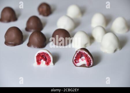 Die Hand der Frau wählt und greift frisch rot und glänzend frisch Himbeeren in hausgemachte schwarze und weiße Schokolade getaucht Stockfoto