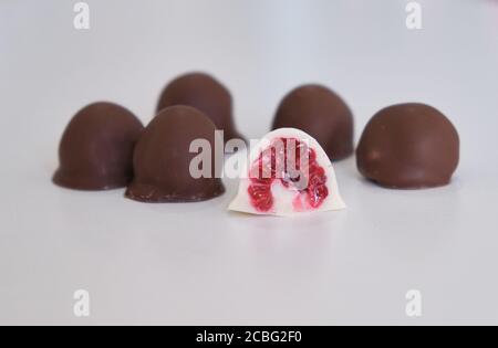 Die Hand der Frau wählt und greift frisch rot und glänzend frisch Himbeeren in hausgemachte schwarze und weiße Schokolade getaucht Stockfoto