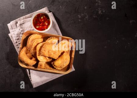 Typisch kolumbianische Empanadas mit würziger Sauce auf schwarzem Hintergrund serviert Stockfoto