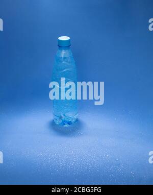Blaue Plastikwasserflasche auf blauem Hintergrund mit Wasser Tropfen Stockfoto