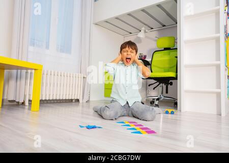 Autistischer Junge mit pädagogischer Übung Entwicklung geometrische Formen schreien Abdeckung Ohren sitzen auf dem Boden Stockfoto