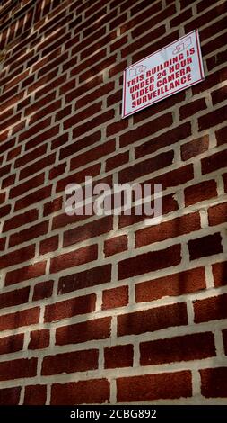 Rote Backsteinmauer mit einem Warnschild, „Dieses Gebäude ist unter 24 Stunden Videoüberwachung“ Stockfoto