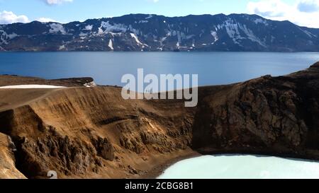 Blick auf den Viti Krater von Krafla Caldera mit geothermaler See (Mit zwei Wanderern) und Berge in der Ferne Stockfoto