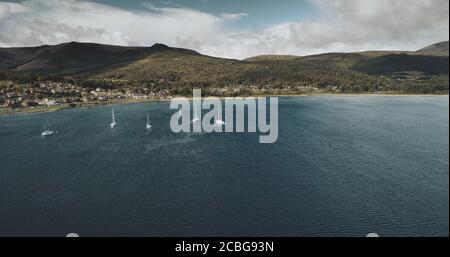 Schottlands Segelboote Meereslandschaft Luftaufnahme im Küstenwasser der Brodick Bay. Schiffe und Boote in der Nähe von Ufer mit Häusern, Hütten, Straßen im Grünen va Stockfoto